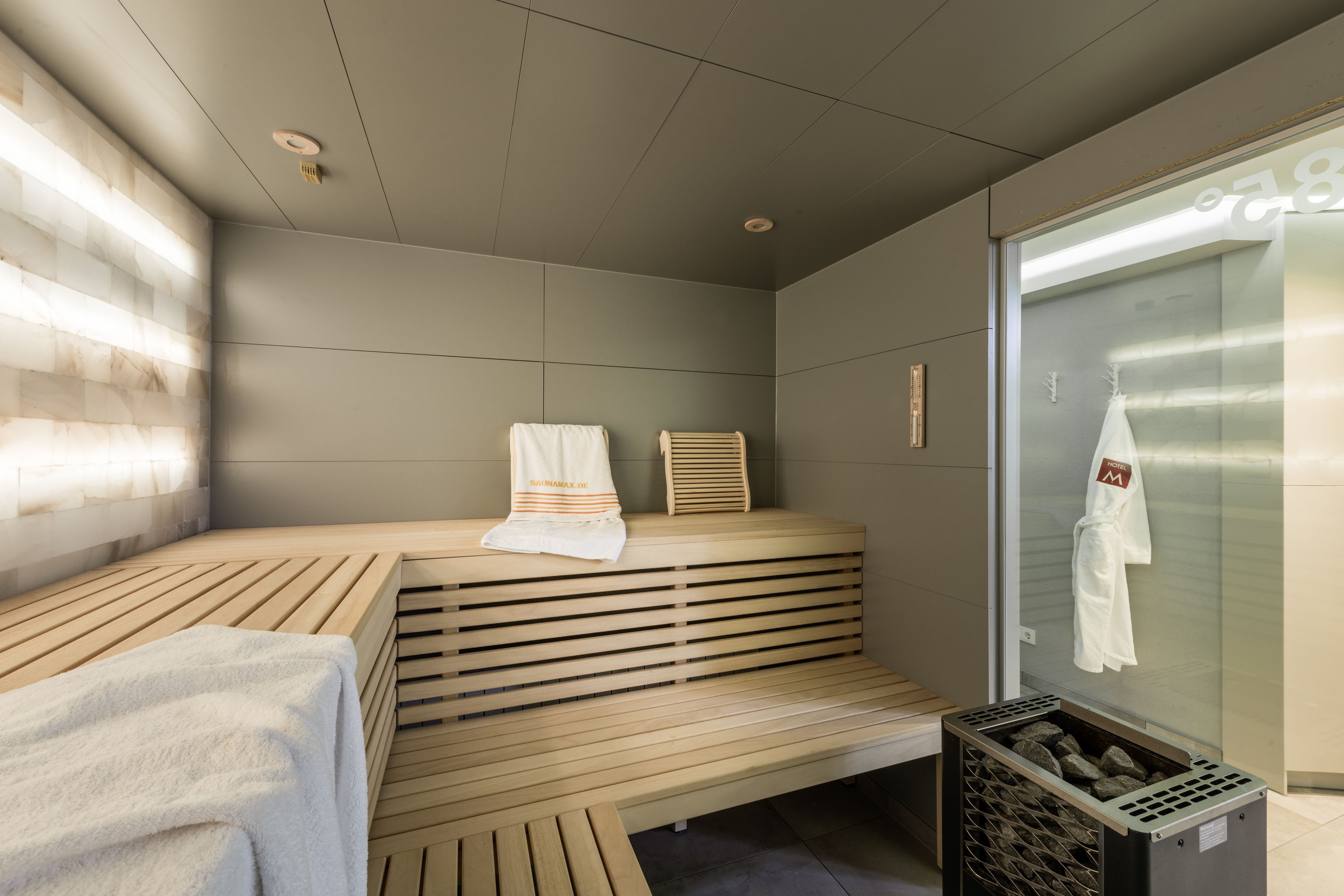 Un sauna moderno con banco de madera, toallas y puerta de cristal.