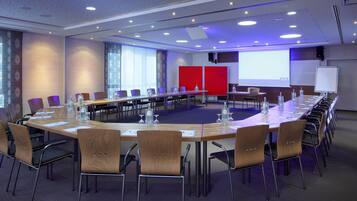 A conference room with a long table, chairs, a projector screen, and a whiteboard.