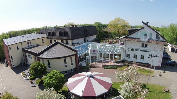 A hotel with a glass conservatory, a restaurant, and a parking area. - Hotel Monika (Buettelborn)