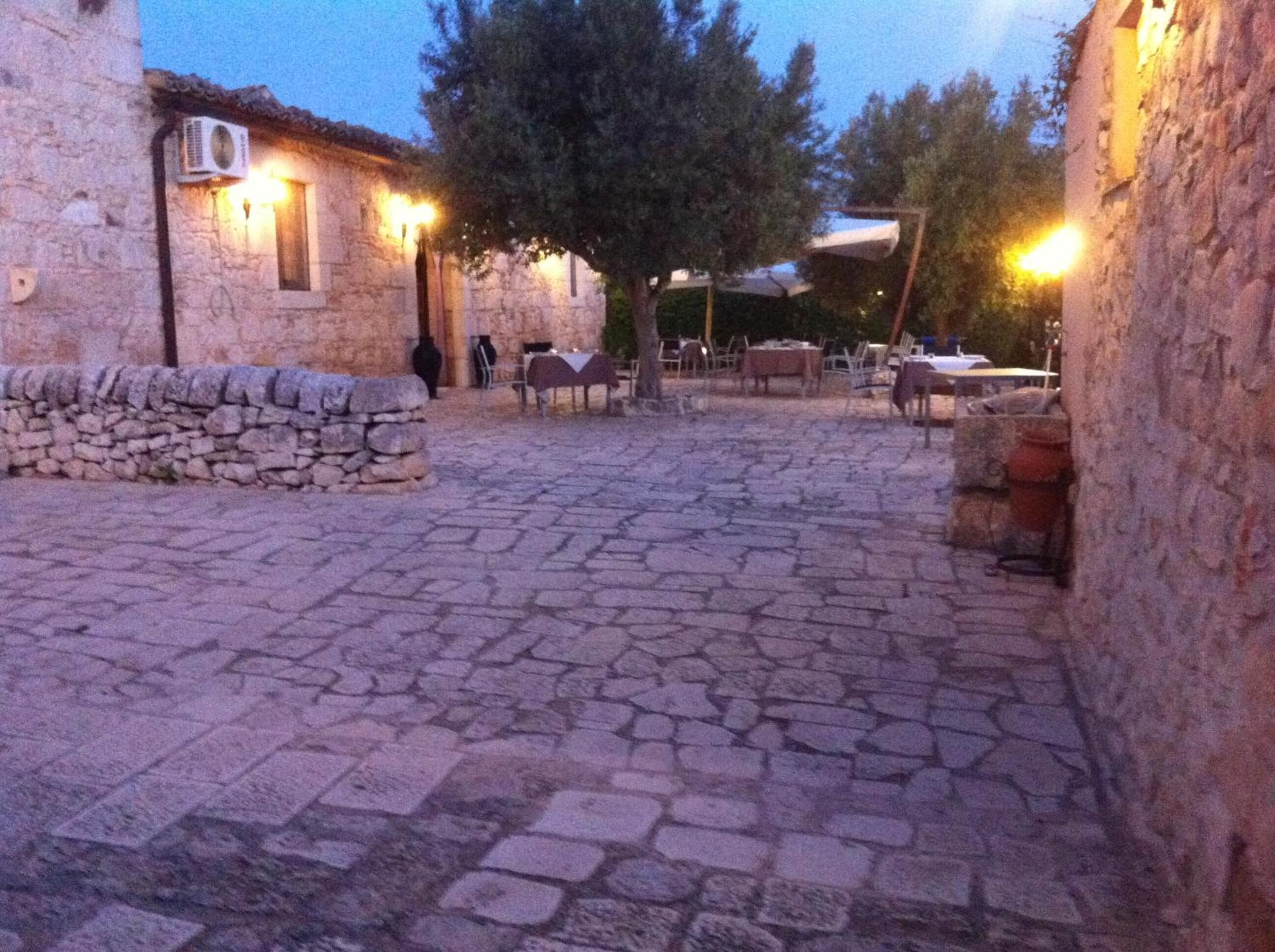 A stone courtyard with tables and chairs, stone walls, and a tree.