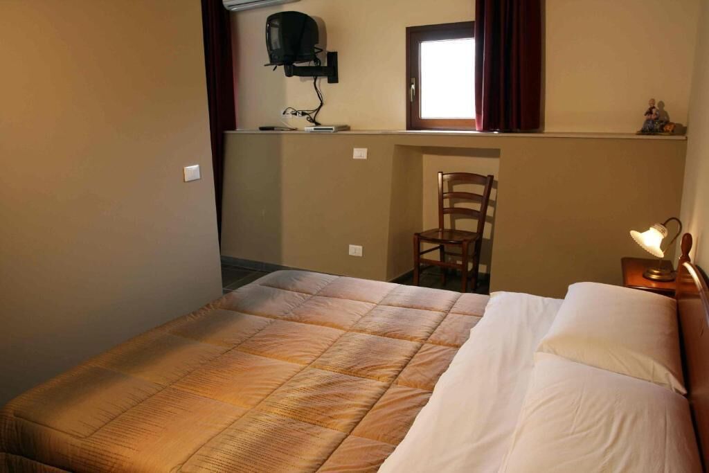 A hotel room with a bed, a chair, a desk with a computer, and a window with curtains.
