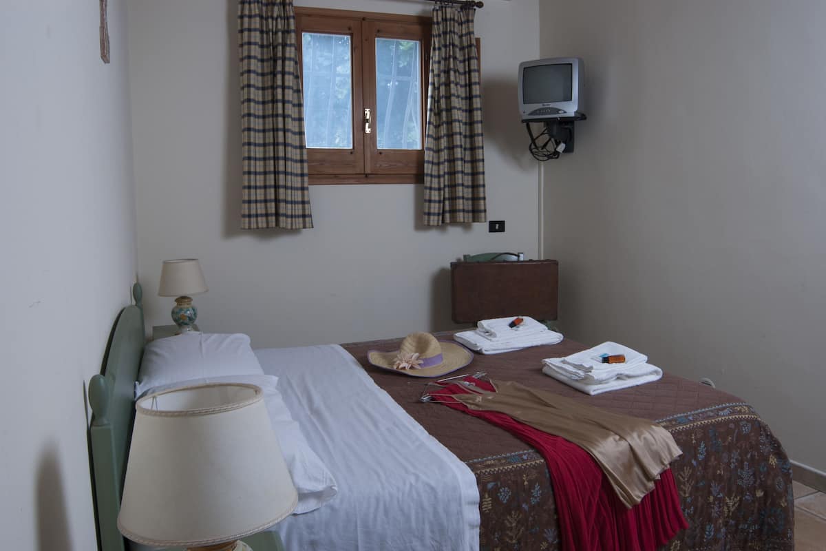 Habitación de hotel con cama, lámpara, televisor y ventana con cortinas.