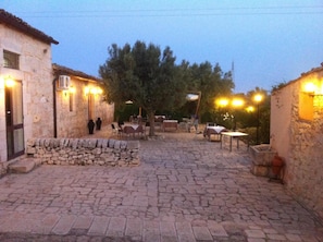 A cobblestone courtyard with stone benches and tables, surrounded by stone buildings with outdoor lighting. - Agriturismo Al Casale (Ragusa)