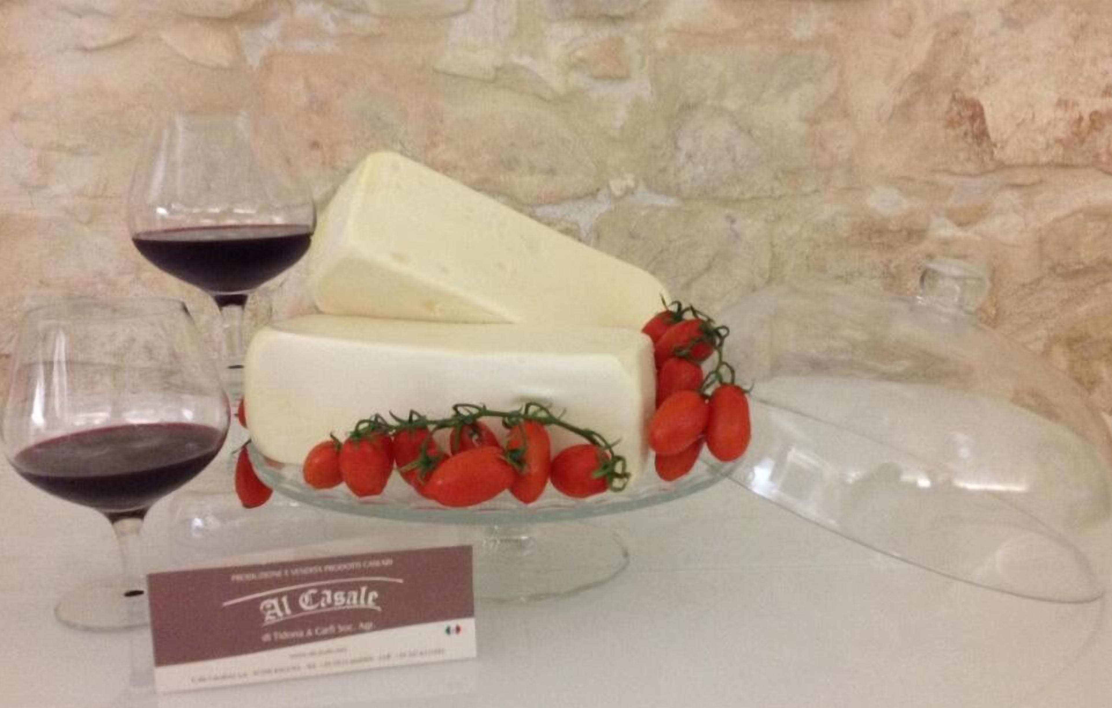 A cheese platter with tomatoes on a glass stand, accompanied by two wine glasses and a sign.