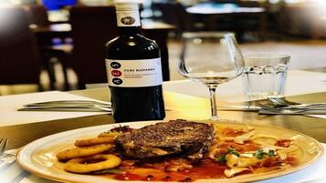 Un plato de comida con un filete, pasta y aros de cebolla, una botella de vino y un vaso de agua sobre una mesa en un restaurante.