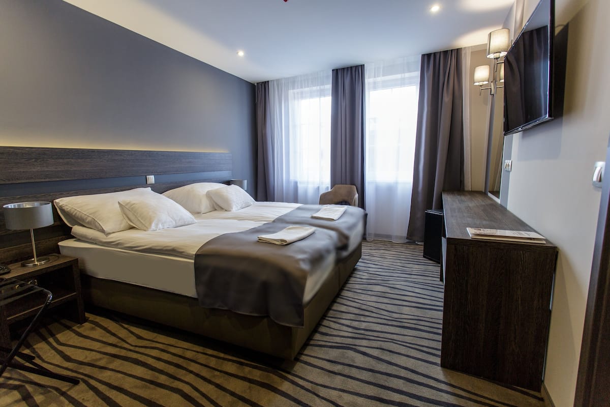 Habitación de hotel con una cama grande, un escritorio, una silla, un televisor de pantalla plana y un ventanal con cortinas.