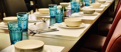 Ein Restaurantambiente mit einem langen Tisch, gedeckt für ein Essen, mit blauem Glas und weißen Tellern.