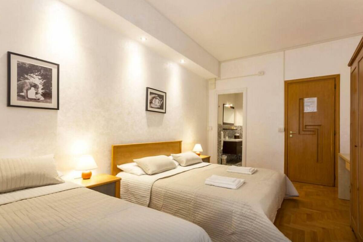 A hotel room with two beds, a wooden door, and framed pictures on the wall.