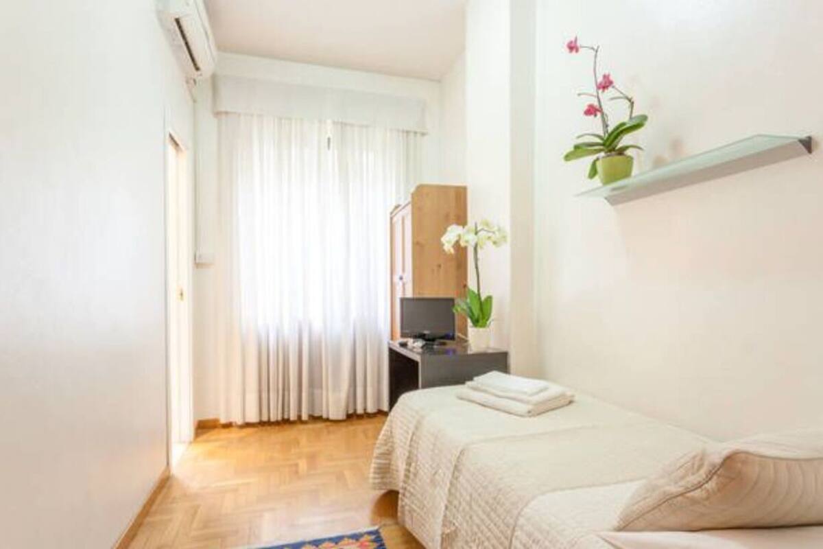 A bedroom with a bed, a TV on a stand, a potted plant, and a window with curtains.