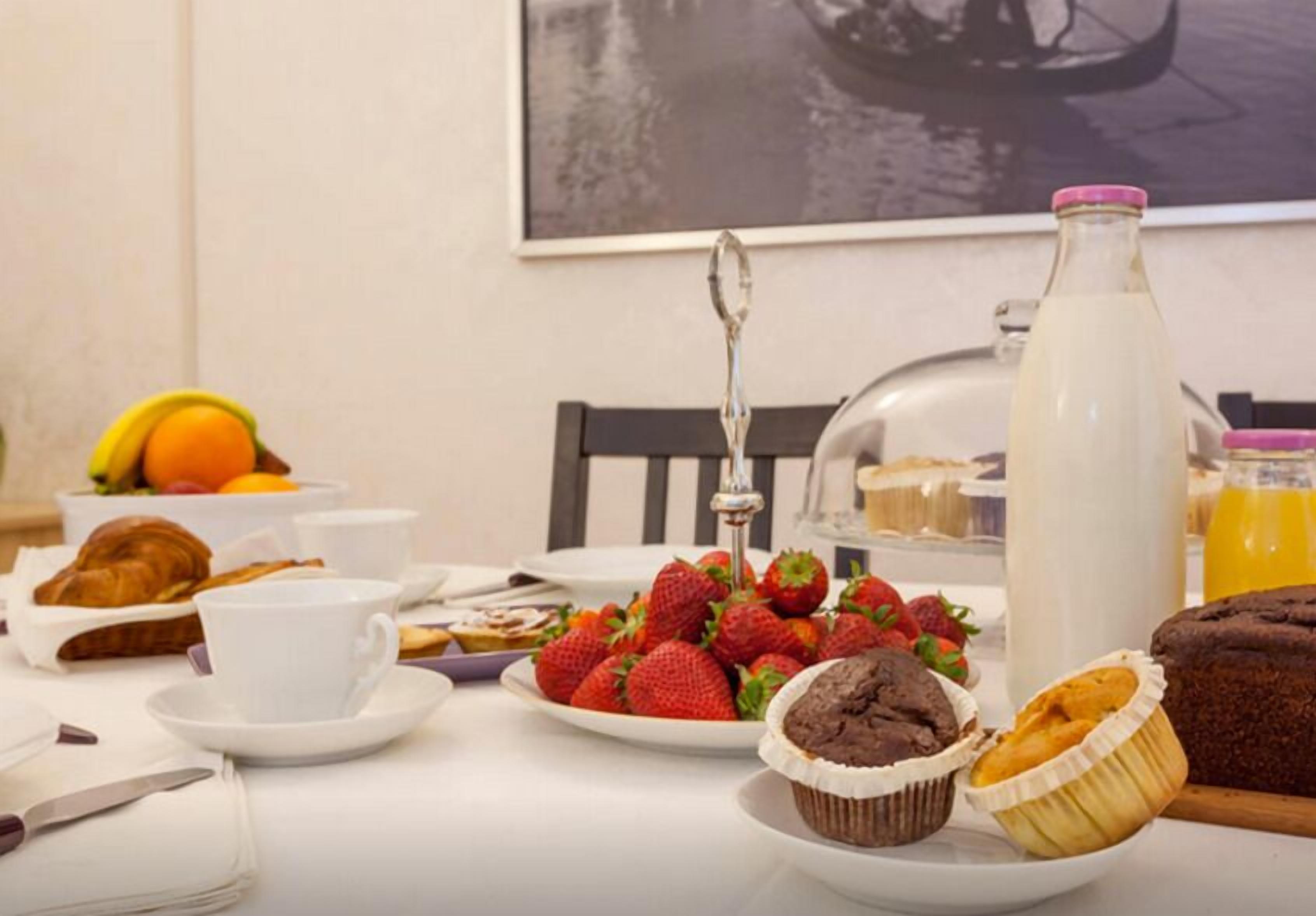 A breakfast table with pastries, strawberries, a milk bottle, and a fruit bowl.