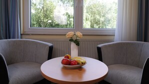 Una habitación con una mesa redonda, dos sillas, un florero con flores y un frutero con fruta.