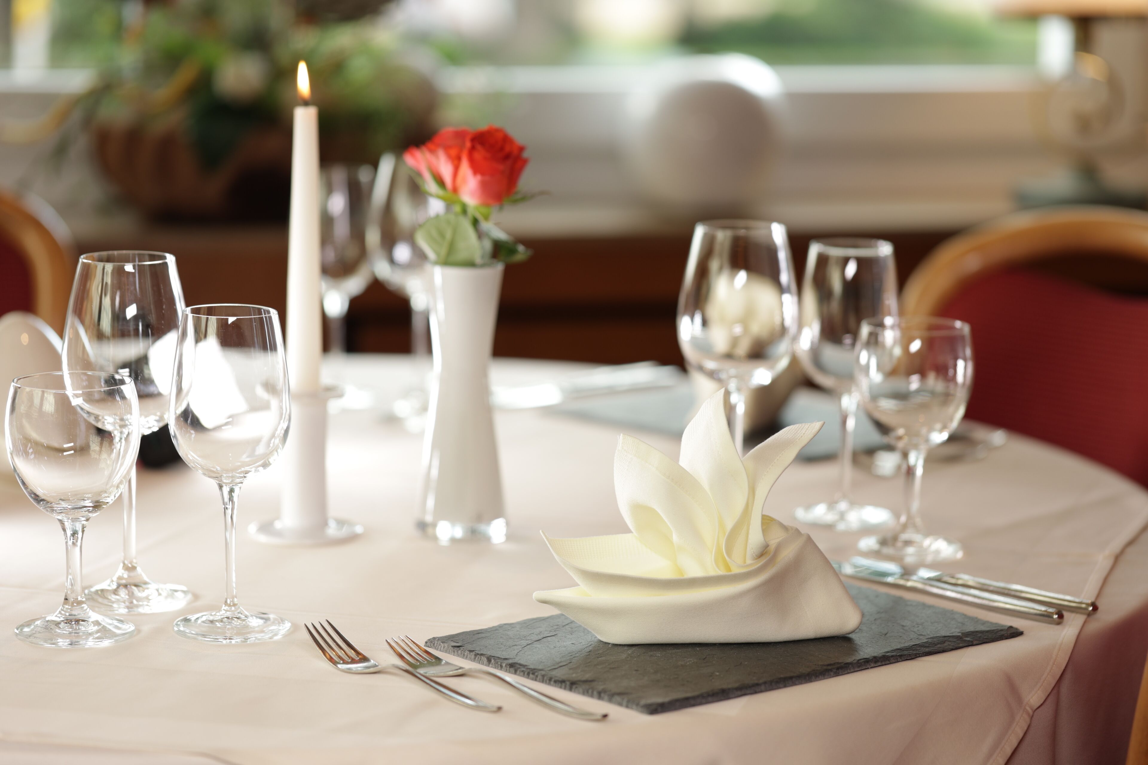A dining table set with wine glasses, a candle, and a white flower arrangement.
