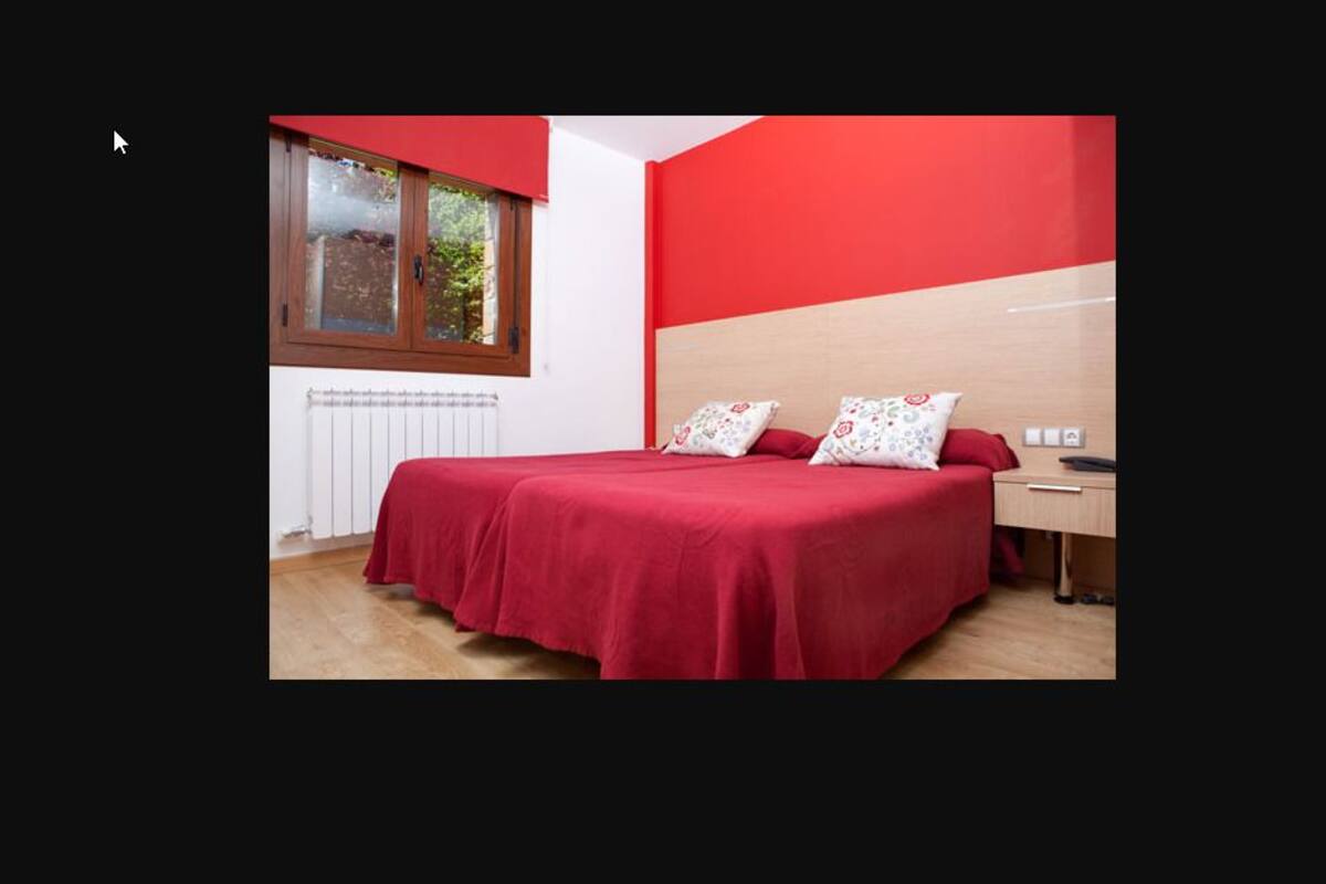 Une chambre avec une couvre-lit rouge, une tête de lit en bois et une fenêtre donnant sur un paysage verdoyant.