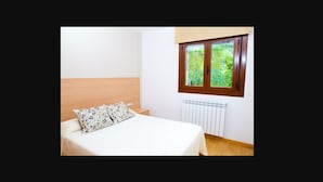Een slaapkamer met een houten hoofdbord, een witte spreidekking, een kussen met een patroon, een raam met uitzicht op groen, en een radiator.