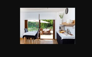 A dining area with a table set for two, a view of the outdoors, and a kitchen area with a clock on the wall. - Apartahotel Castejón de Sos (Castejon de Sos)