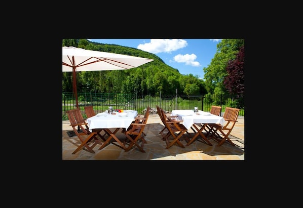 An outdoor dining area with tables and chairs, a large umbrella, and a scenic mountain backdrop.