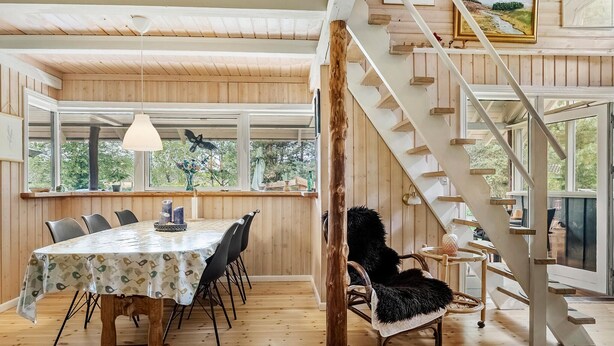 A dining area with a table set for six, wooden flooring, a staircase, and large windows offering a view of greenery outside. - Awesome home in Hovborg with WiFi (Hovborg)
