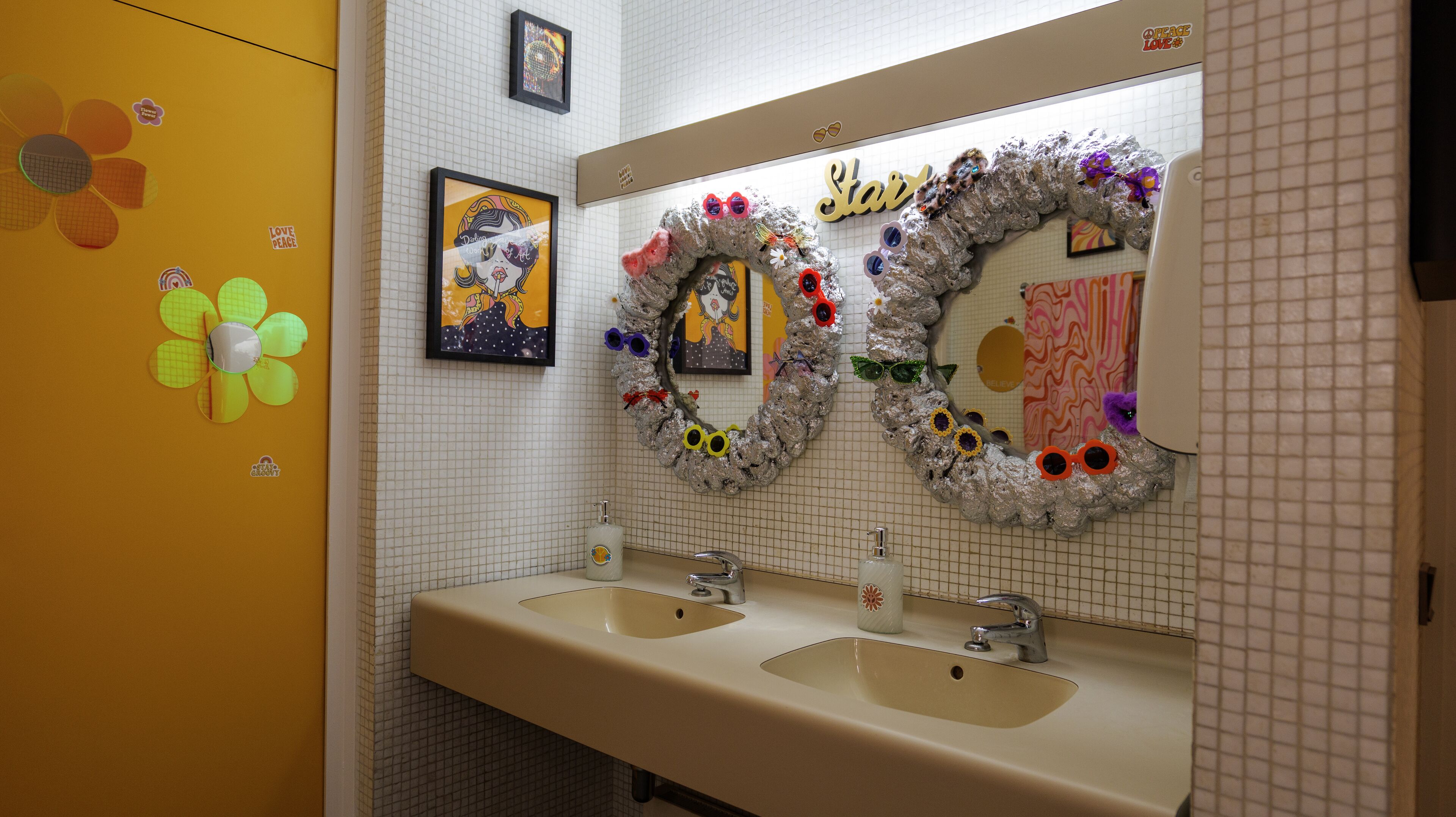 Een badkamer met twee wastafels, een spiegel en een gele wand met bloemdecoraties.