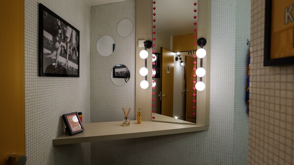Un baño con espejo, iluminación y un cuadro en la pared.