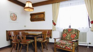 A dining area with a wooden table and chairs, a floral-patterned armchair, a hanging lamp, and a radiator. - Pension Baranek (Kaprun)