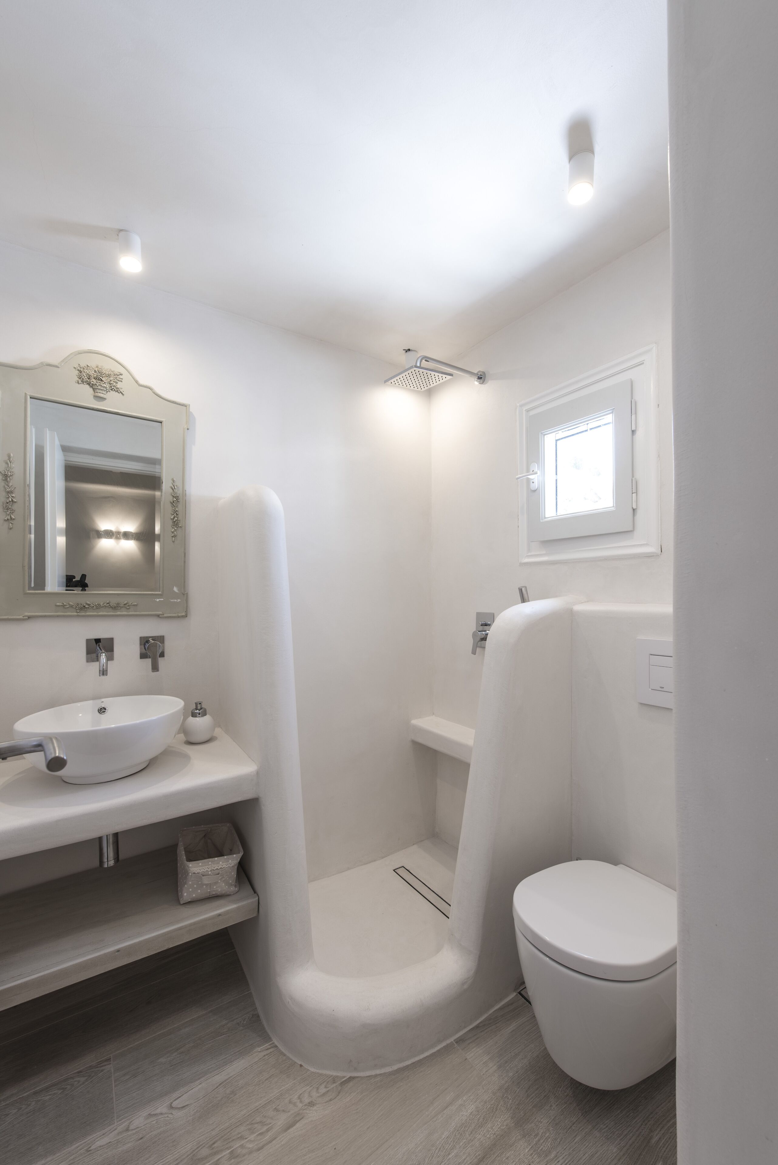 Et moderne badeværelse med en hvid vask, spejl, bruser og toilet.