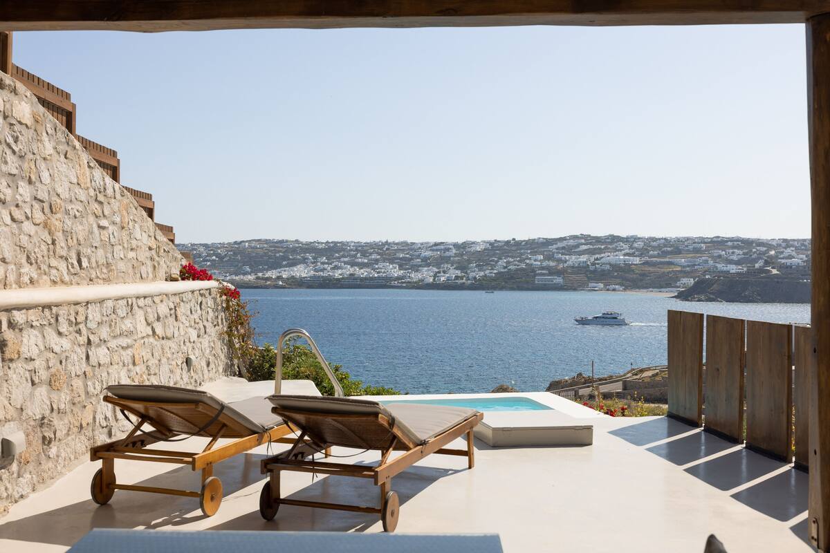 A stone wall with a pool and lounge chairs overlooking a coastal cityscape.