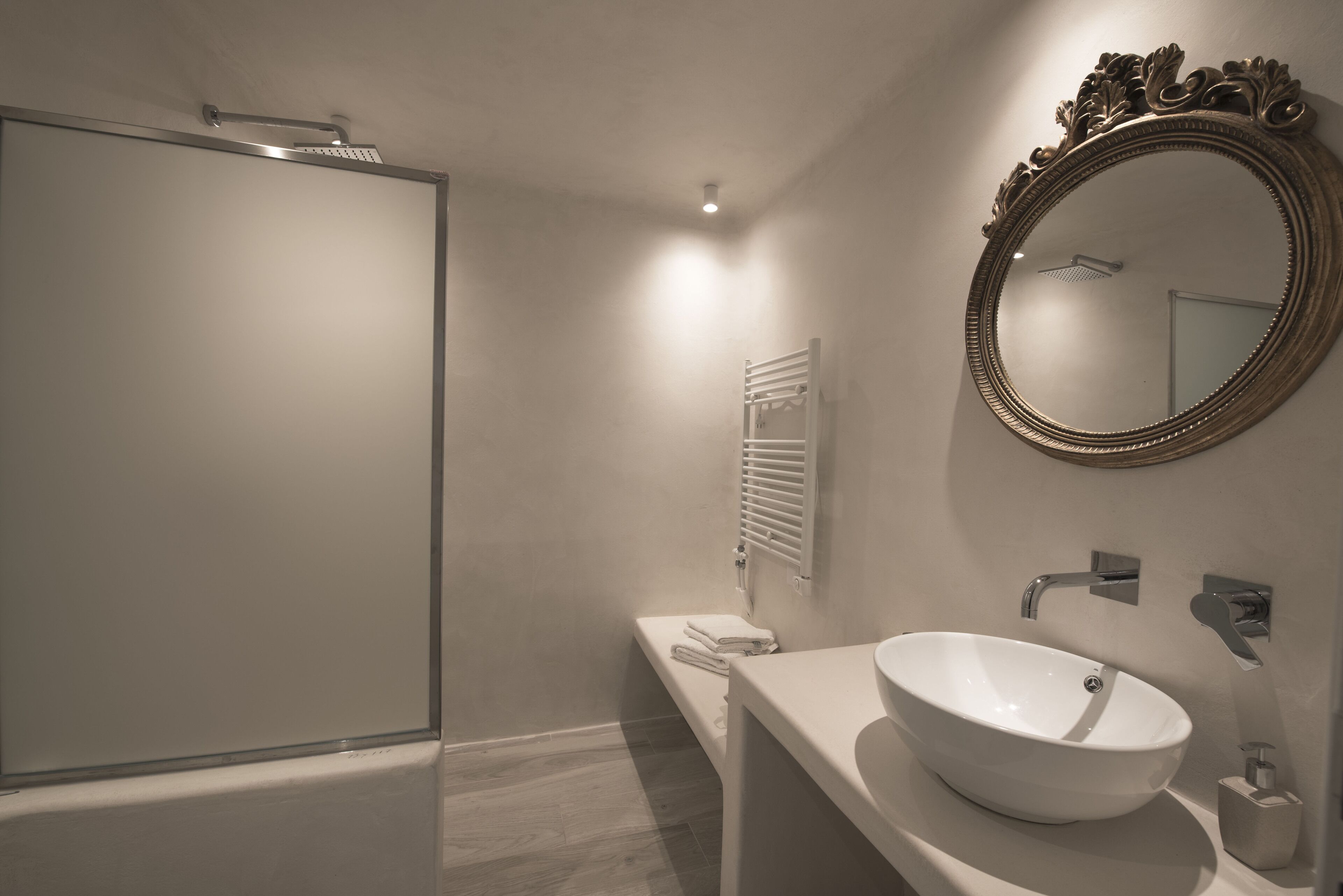 A modern bathroom with a glass shower enclosure, a white sink with a vessel basin, and a large ornate mirror on the wall.