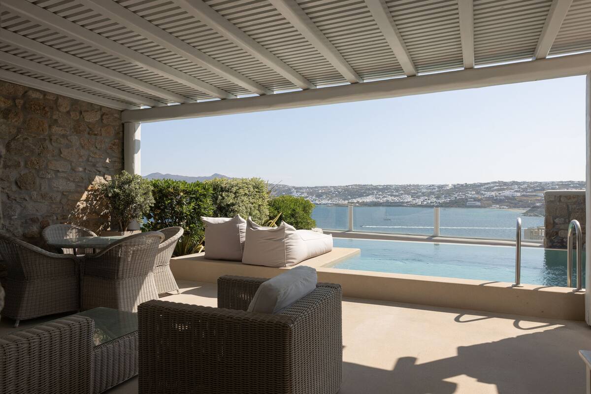 A terrace with wicker furniture, a pool, and a view of the sea and cityscape.