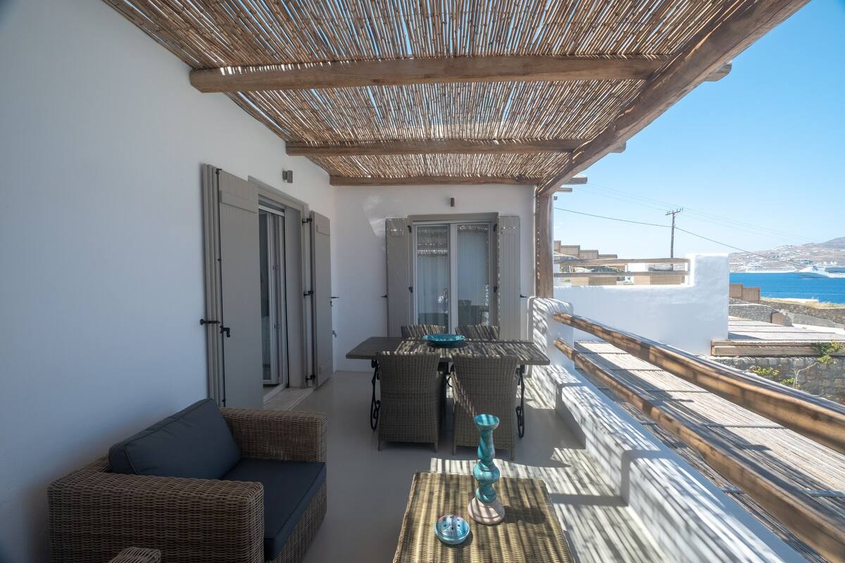 A balcony with wicker furniture, a table, and a view of the sea.