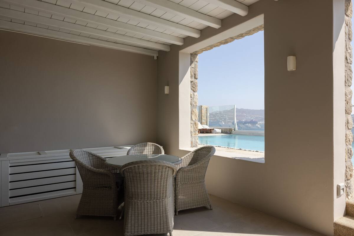 A sunlit patio with wicker furniture, a view of a pool, and a stone wall.