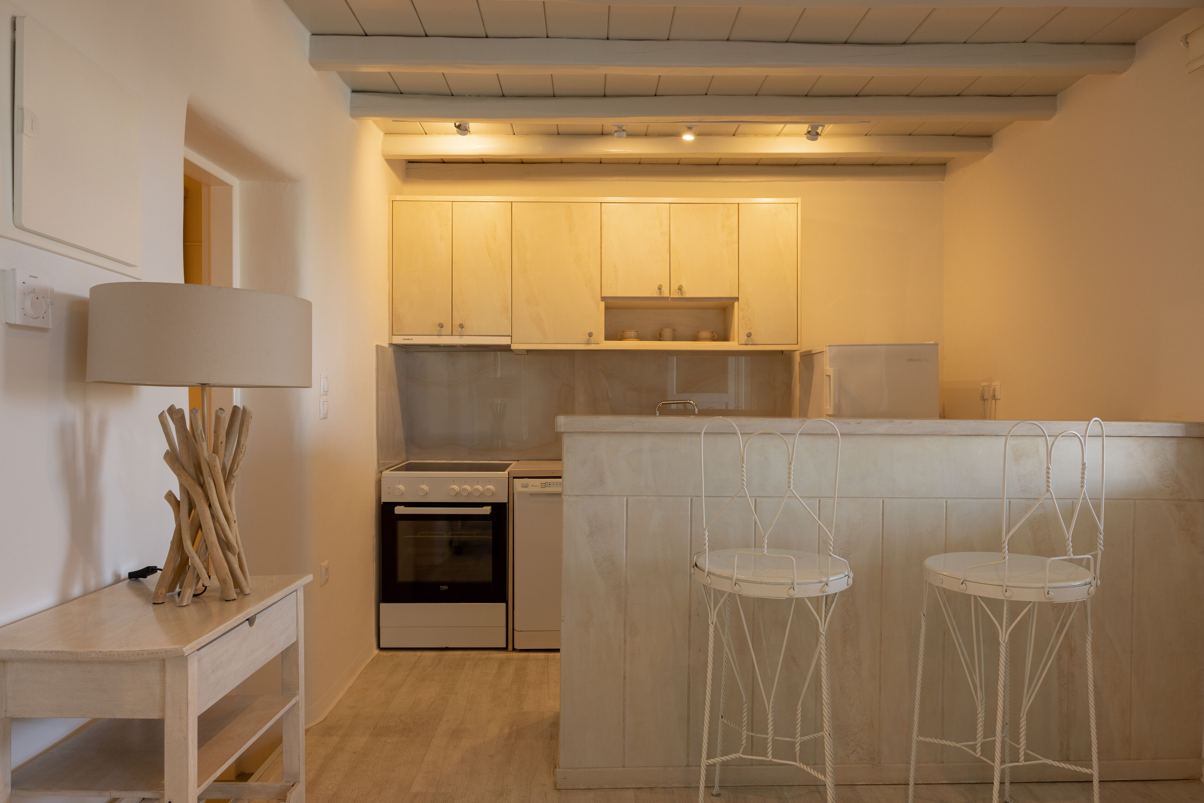 A compact kitchen with white cabinetry, a built-in oven, a dishwasher, and a bar area with two stools.
