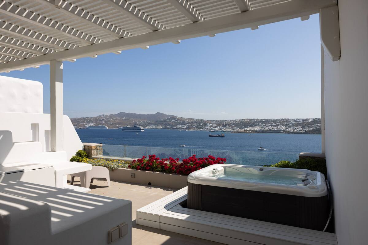 A terrace with a hot tub, white furniture, and a view of the sea and distant mountains.