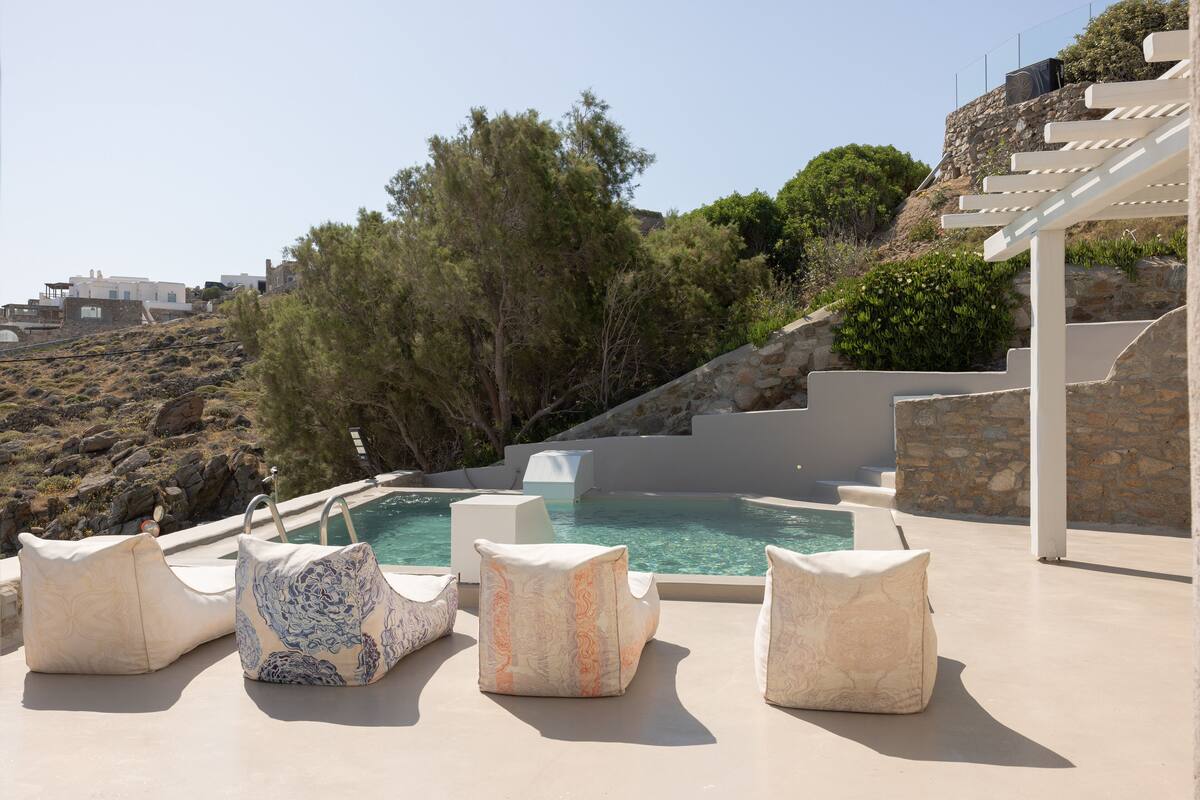 A poolside area with outdoor seating and a view of a hillside.