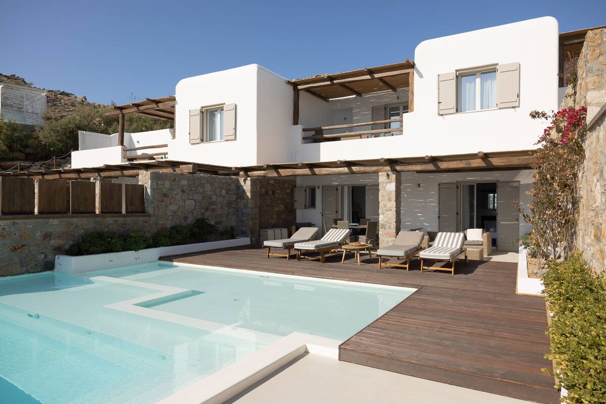 A modern villa with a swimming pool, outdoor seating, and a stone retaining wall.