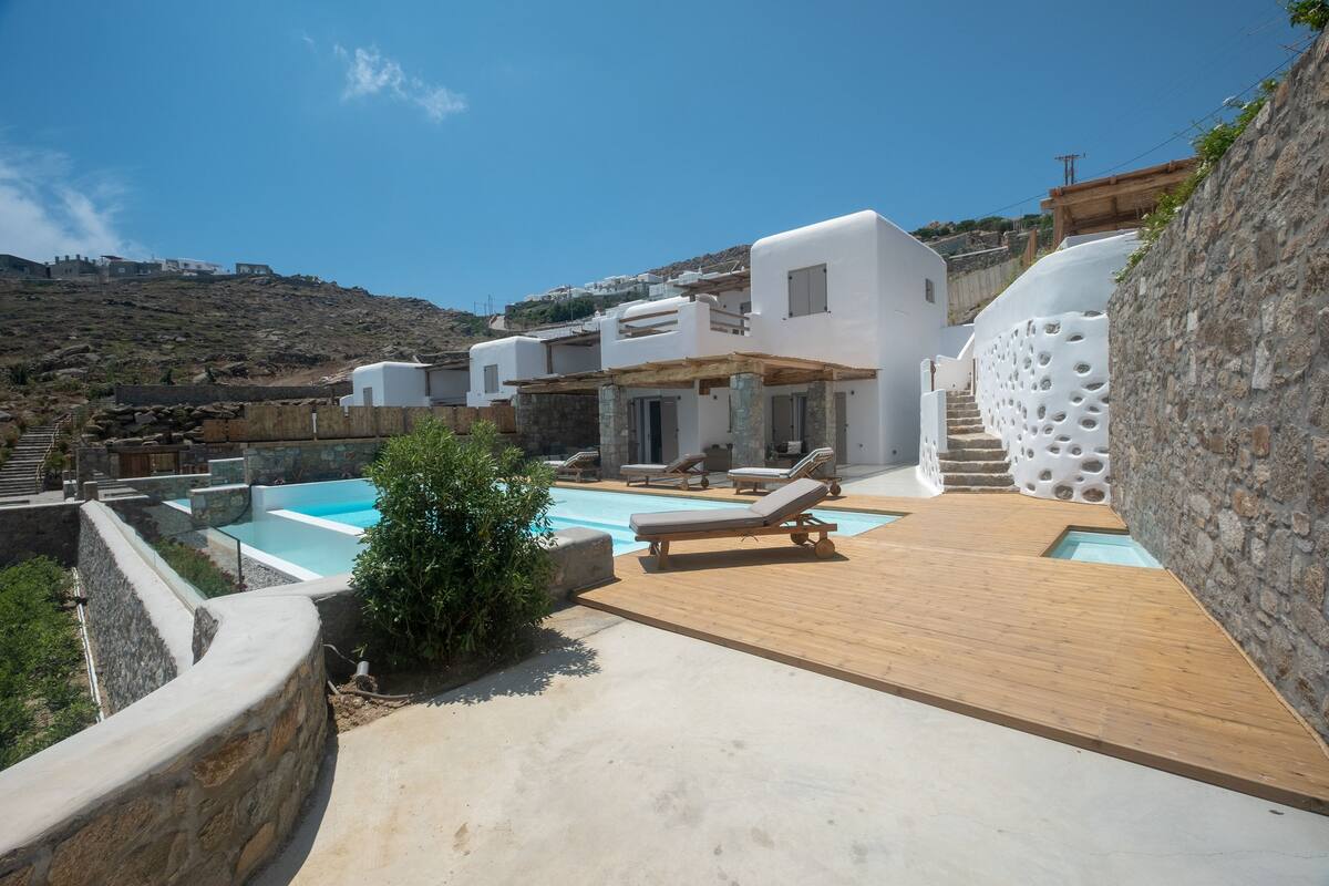 A modern villa with a swimming pool, wooden deck, and stone walls.
