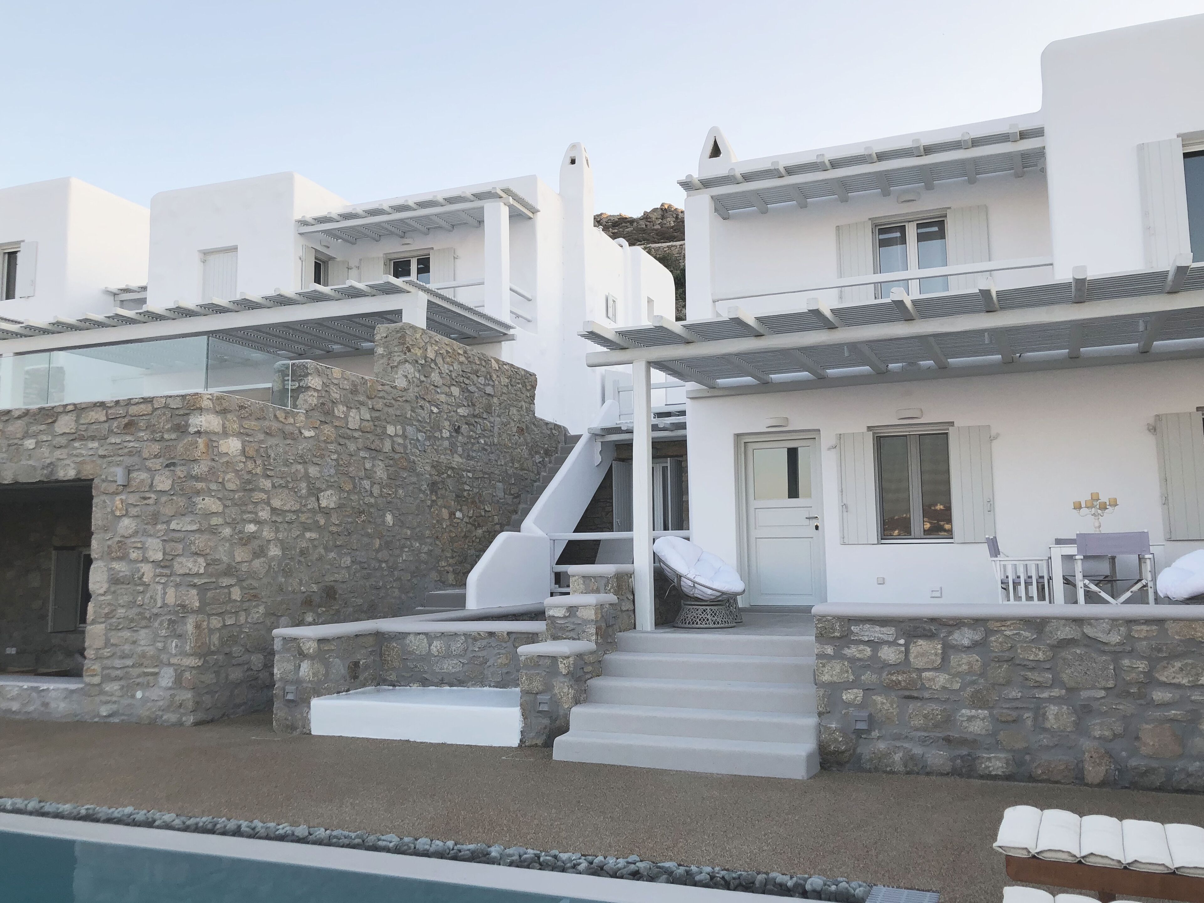 A white building with a stone wall, a staircase, and a pool.