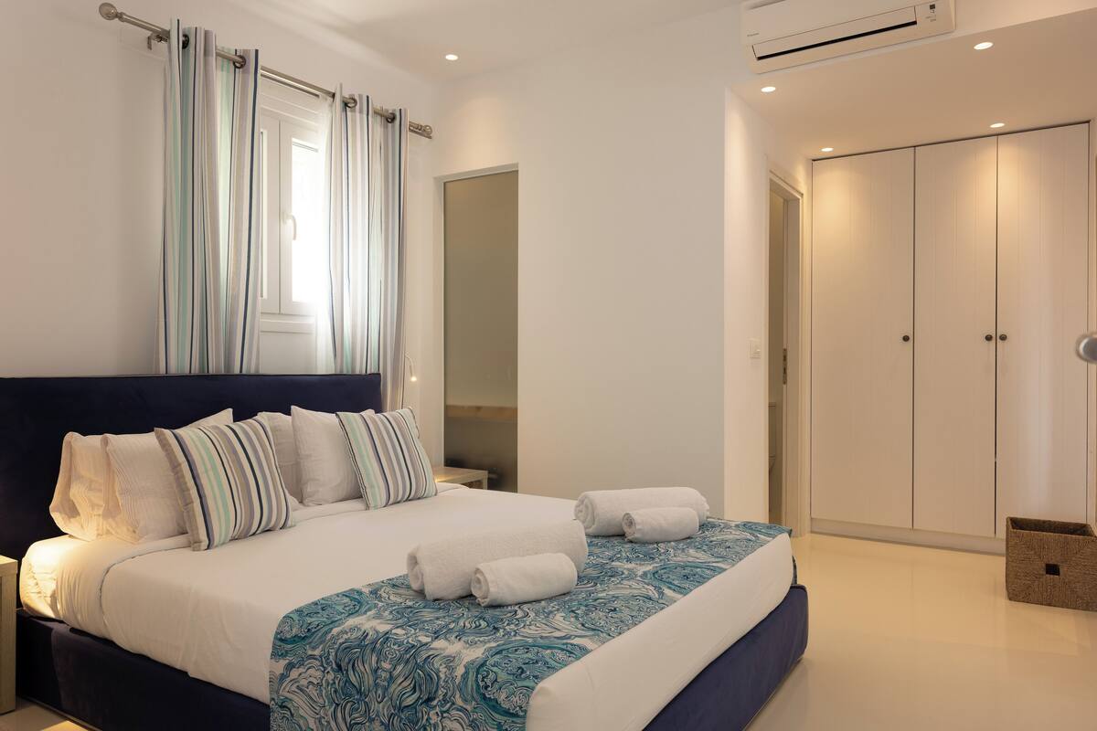 A modern bedroom with a large bed, striped curtains, a wardrobe, and a small basket.