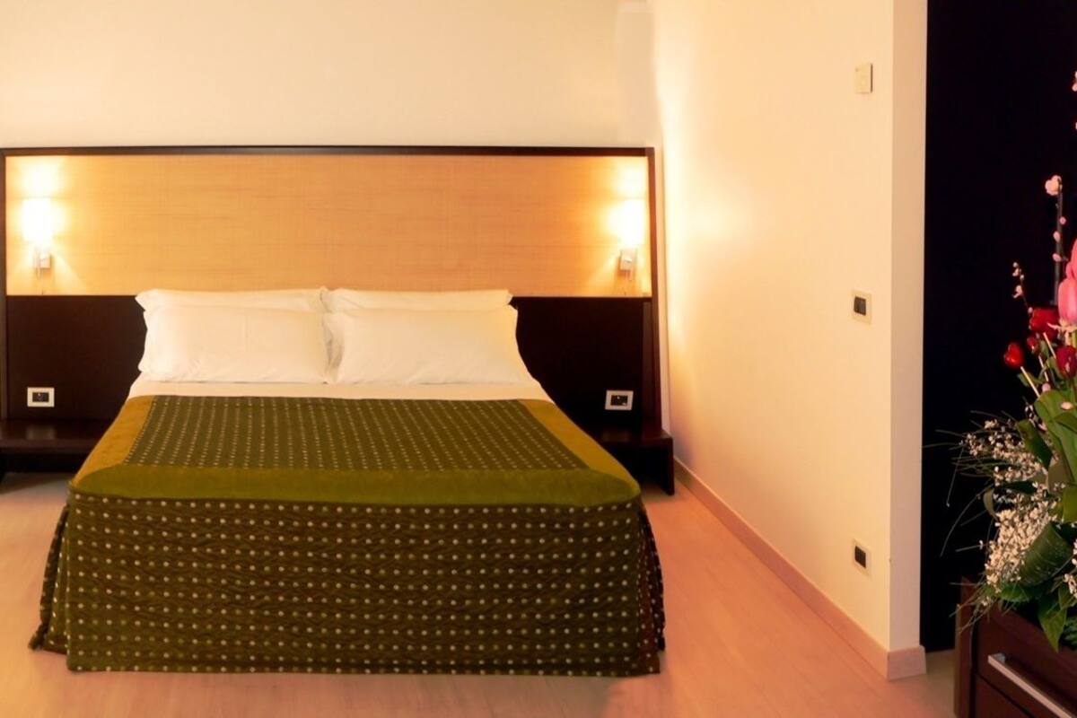 A hotel room with a bed, bedside tables, a nightstand, a potted plant, and a breakfast setup on the floor.