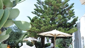 Un espacio exterior moderno con una escultura blanca, un árbol grande y una zona de estar bajo una marquesina.