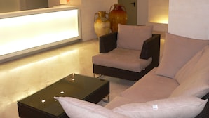 Un área de estar moderna con una mesa de centro de vidrio, dos sillones acolchados y un mostrador de recepción.