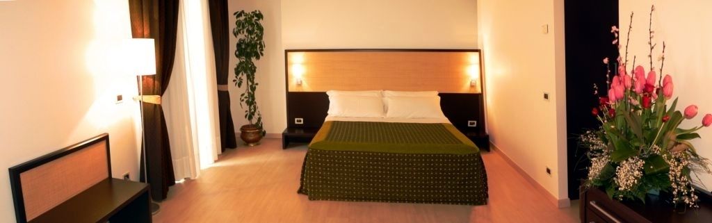 Et hotelværelse med seng, sengeborde, en lampe, en potteplante og en blomsterdekoration.