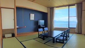 Ein Zimmer mit Tatami-Matten, einem Tisch, Stühlen, einem Fernseher und Blick auf das Meer.