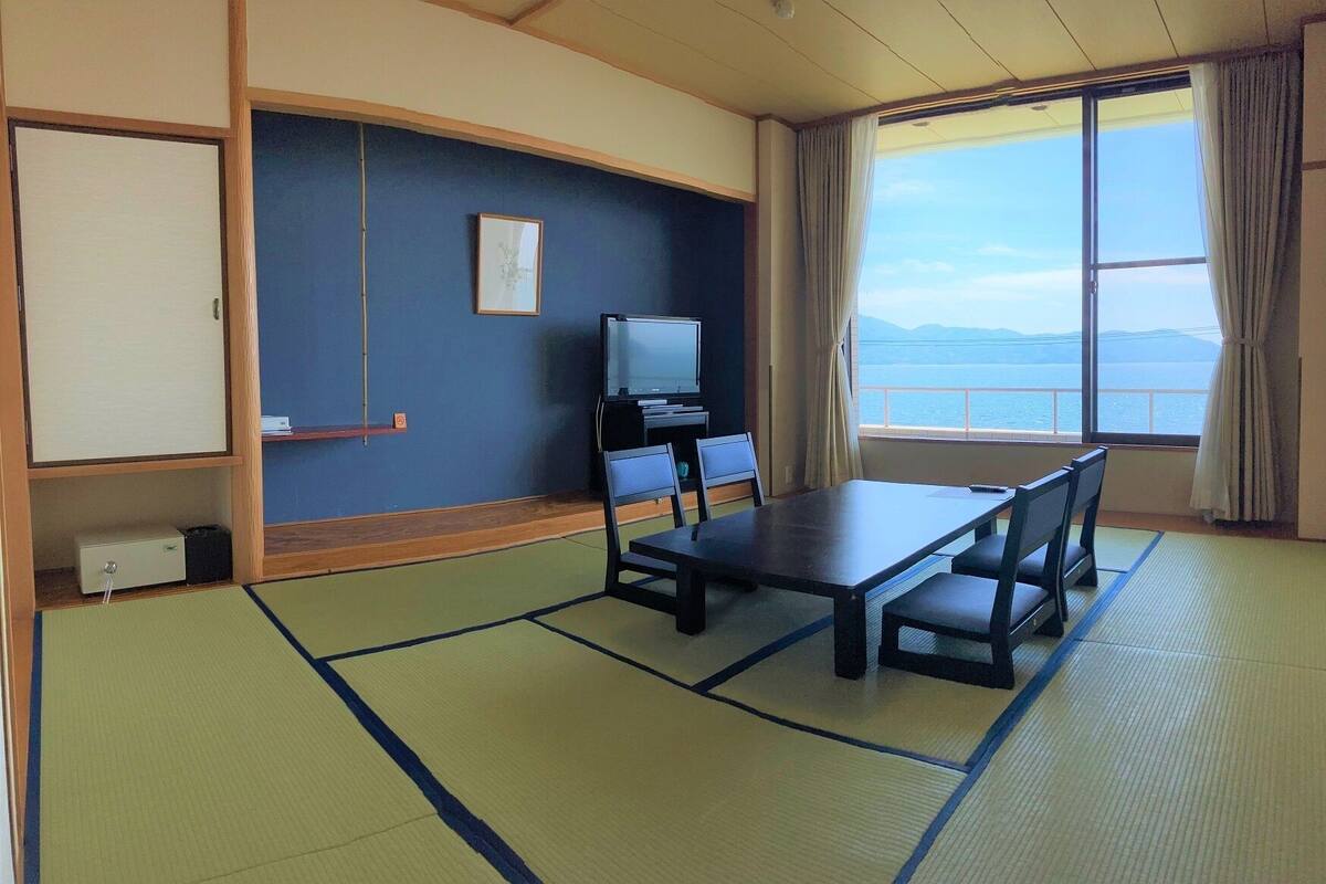 Una habitación con esteras de tatami, una mesa, sillas, un televisor y vista al mar.