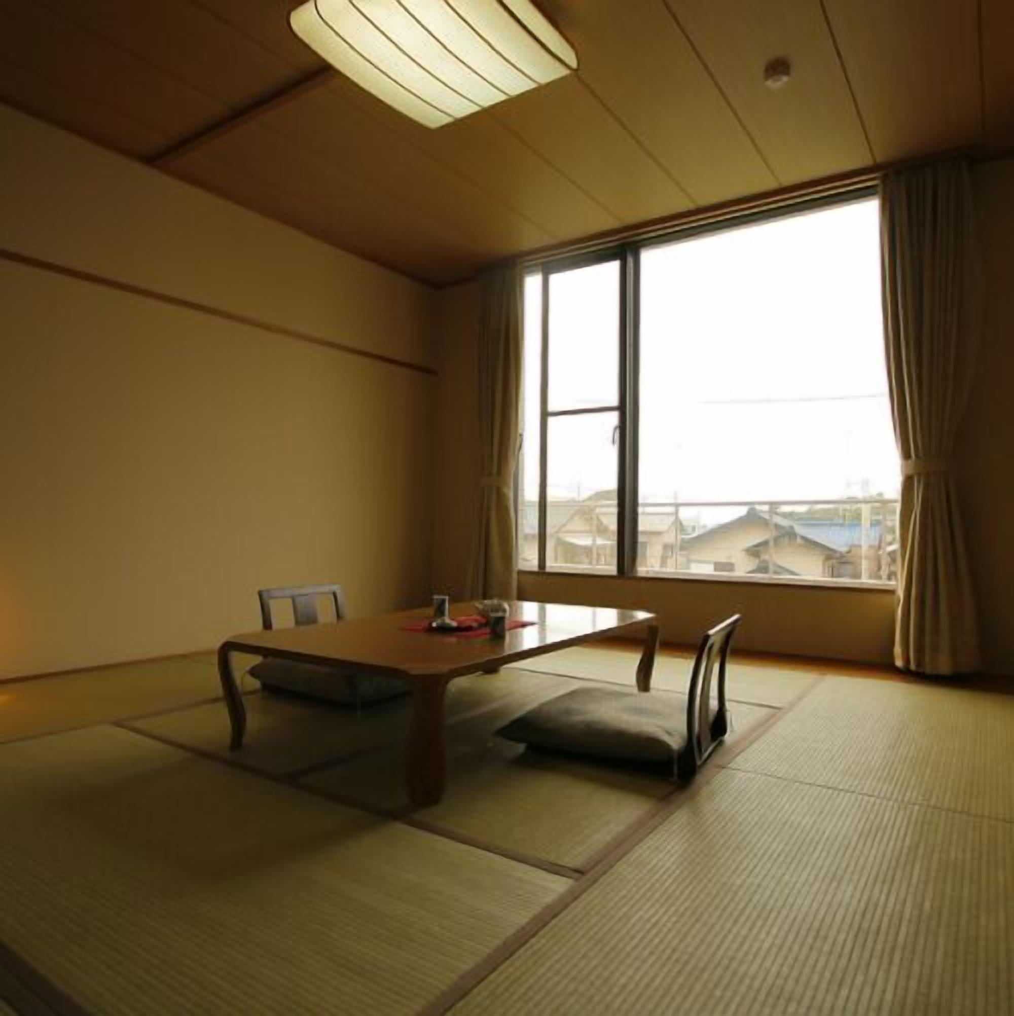 Una habitación japonesa tradicional con suelo de tatami, una mesa baja y un gran ventanal con cortinas.
