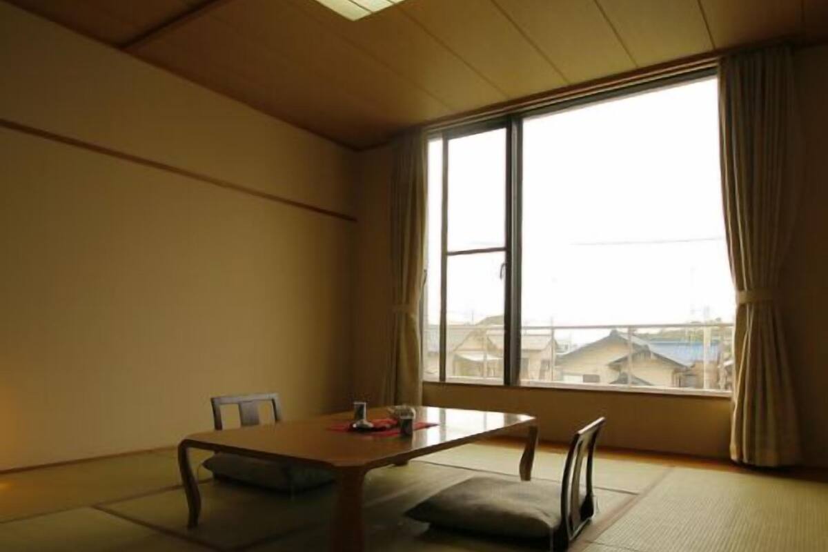 Una habitación japonesa tradicional con suelo de tatami, una mesa baja y un gran ventanal con cortinas.
