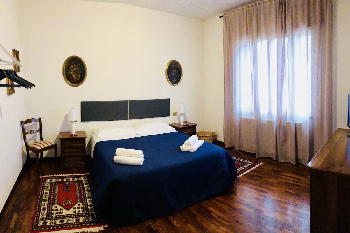 A hotel room with a bed, two bedside tables, a chair, a television, and a window with curtains.