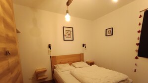 A bedroom with a wooden bed, two bedside tables, a small wooden stool, and two framed pictures on the wall. - Luxury Apartment for 6 - Terrace - Montgenèvre (Montgenèvre)