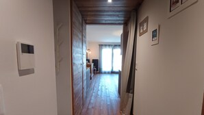 A narrow hallway with wooden flooring, a white wall with a thermostat, and a door leading to a room with a window and curtains. - Luxury Apartment for 6 - Terrace - Montgenèvre (Montgenèvre)