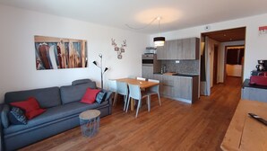 A modern living room with a grey sofa, a round coffee table, and a dining area with a wooden table and chairs. - Luxury Apartment for 6 - Terrace - Montgenèvre (Montgenèvre)