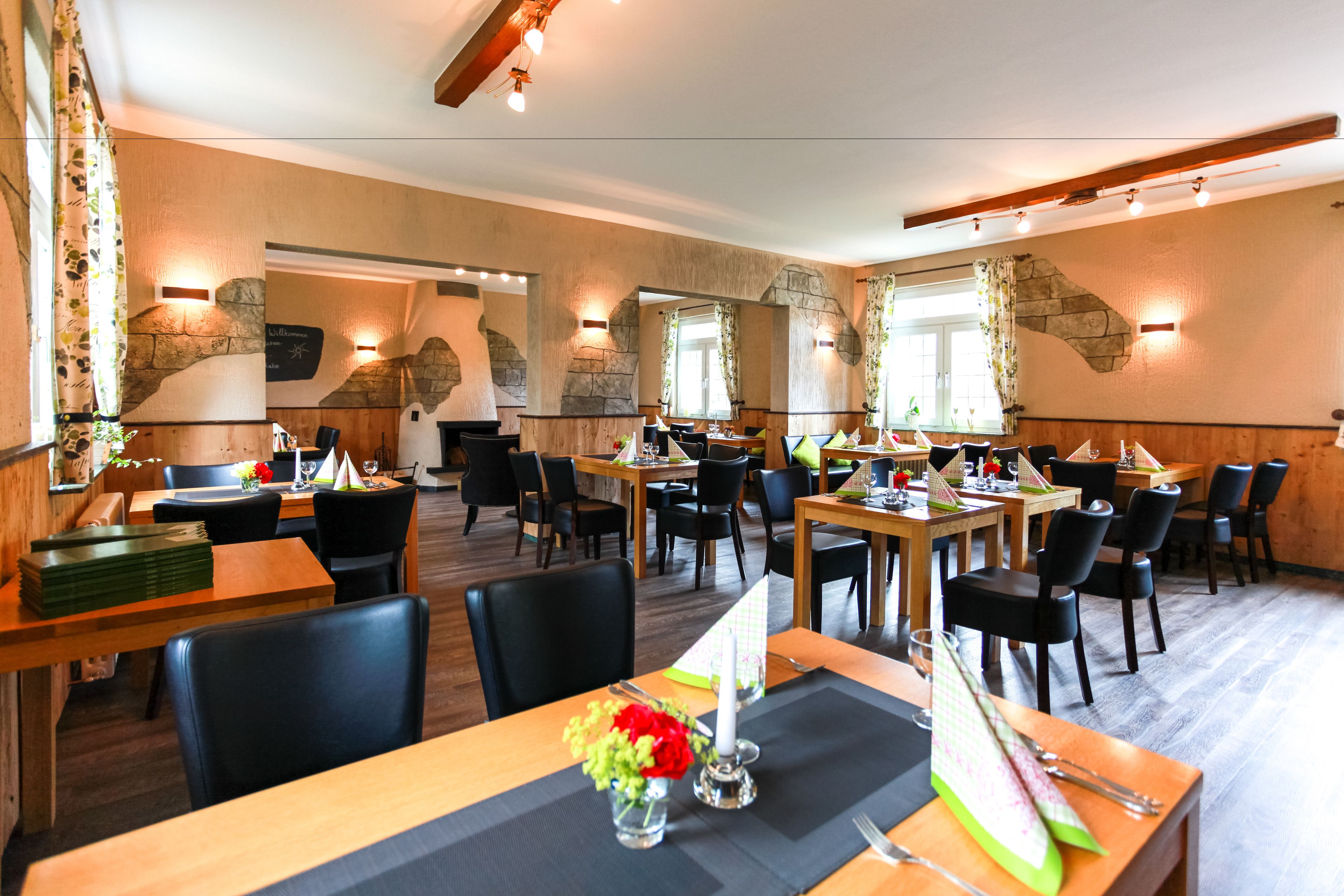 A restaurant with multiple tables and chairs, stone wall accents, and warm lighting.